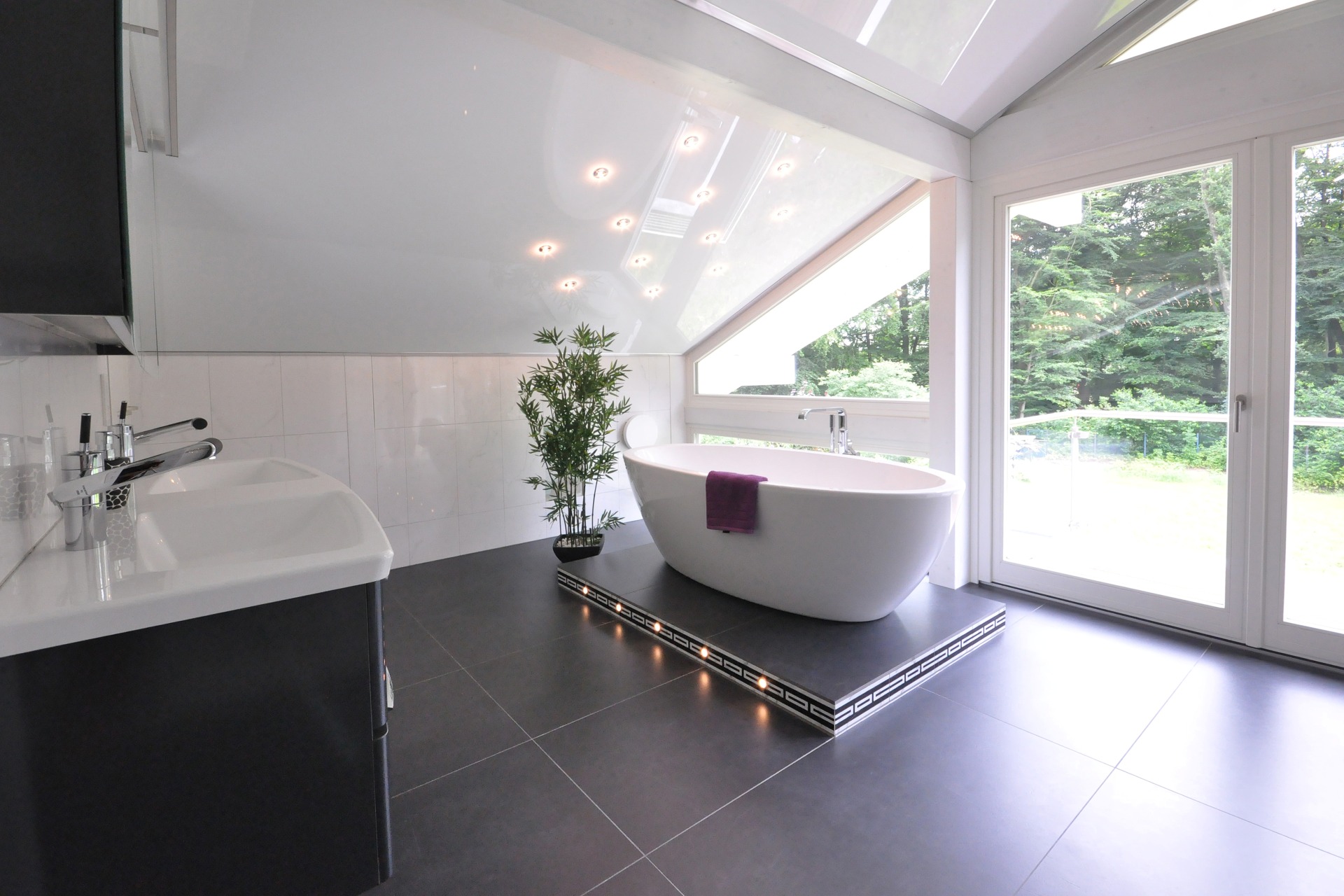 Ein modernes Badezimmer mit freistehender Badewanne, großem Waschtisch und Panoramafenster in einen Garten.