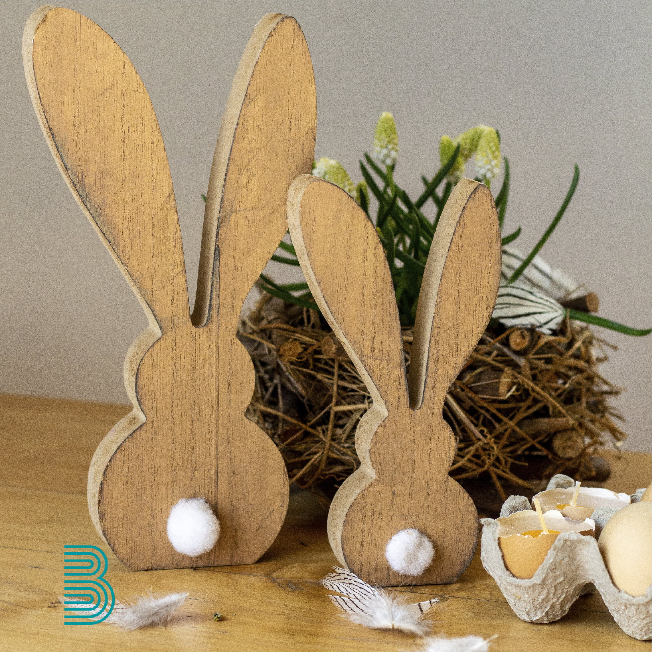 Zwei Osterhasen aus Holz stehen auf einem Tisch vor einem Frühlingsblüher im Korb.