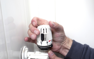 Eine Hand dreht an einem Heizkörperthermostat.