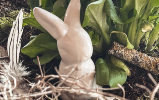 Eine DEkoosterhase steht inmitten österlichem Gesteck.