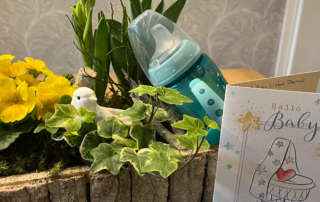 Baby-Geschenk mit Flasche und Blumen.