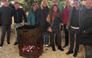 Menschen stehen um eine Feuertonne und lachen in die Kamera.