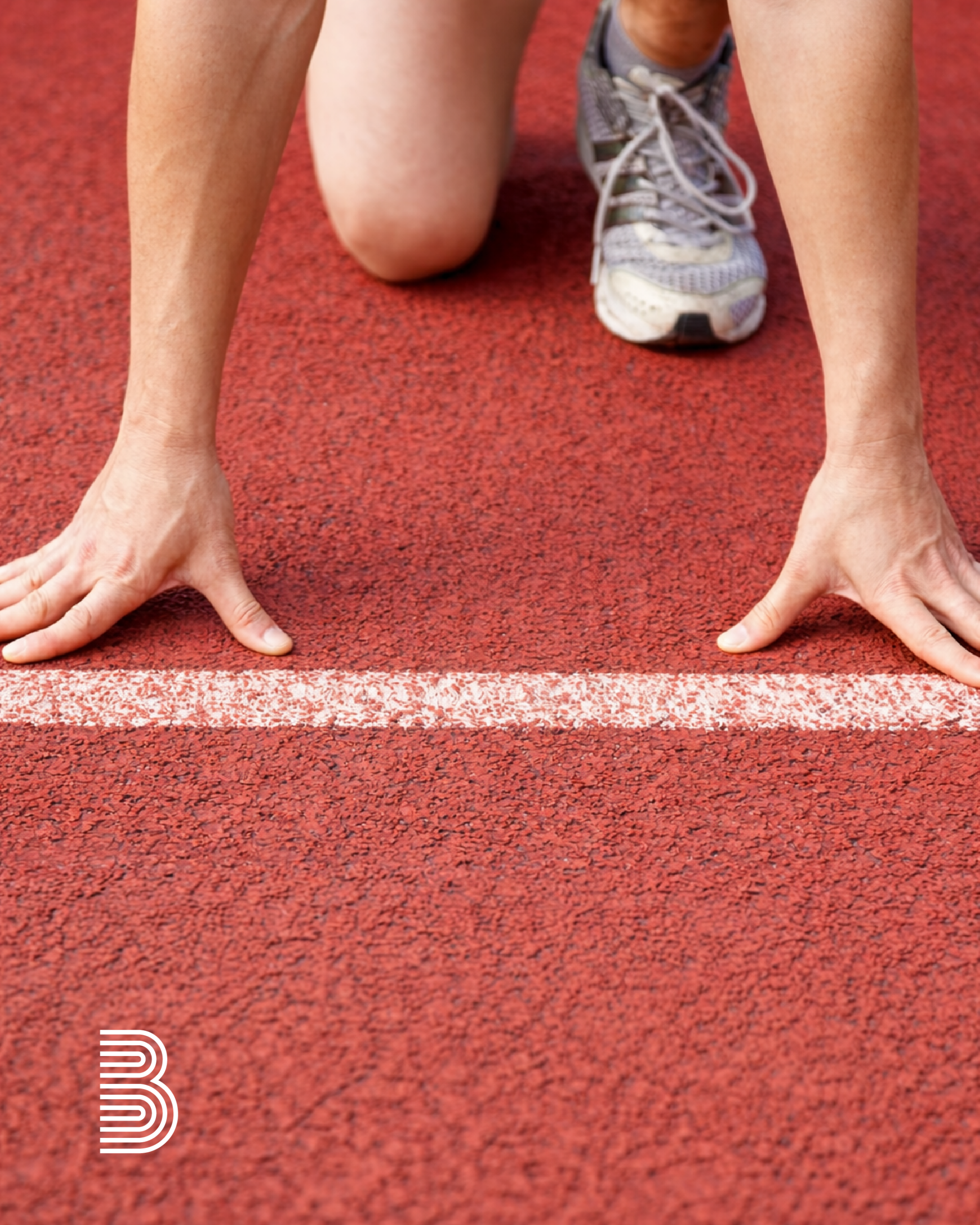 Zwei Hände an einer Startlinie einer Aschbahn.
