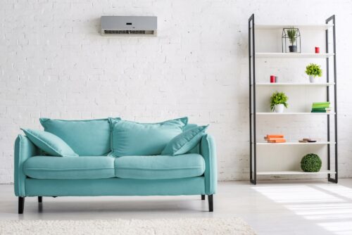 Eine türkisfarbene Couch steht unter einem Klimagerät in einem Wohnraum.