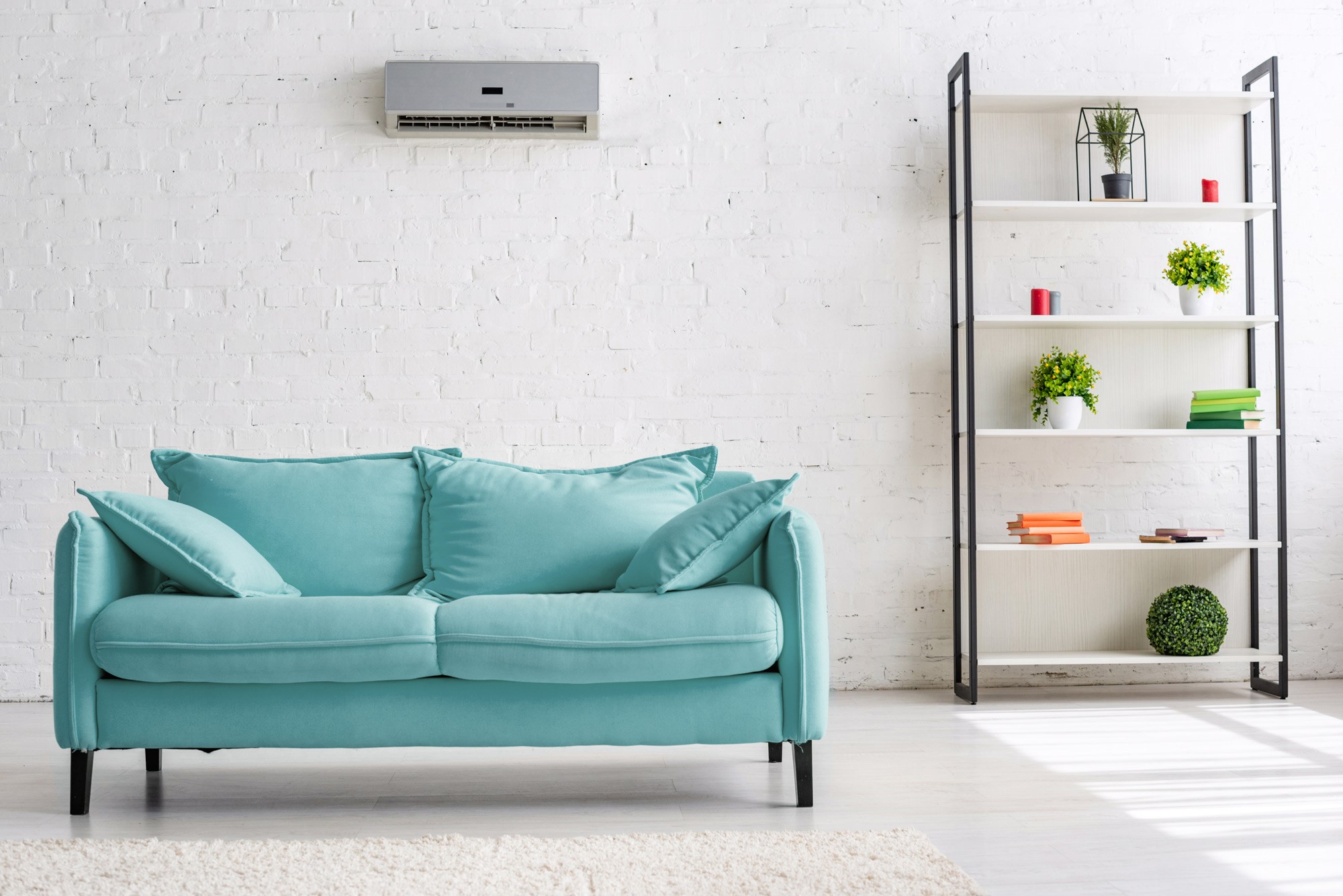 Eine türkisfarbene Couch steht unter einem Klimagerät in einem Wohnraum.