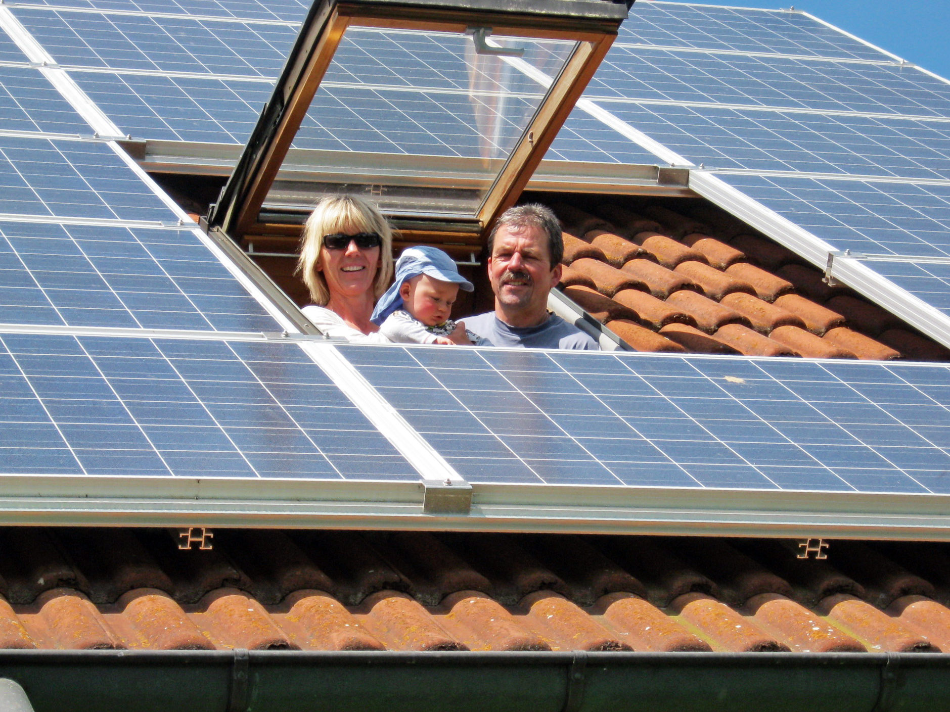 Eine dreiköpfige Familie schaut aus einem Dachflächenfenster auf Solarplatten.