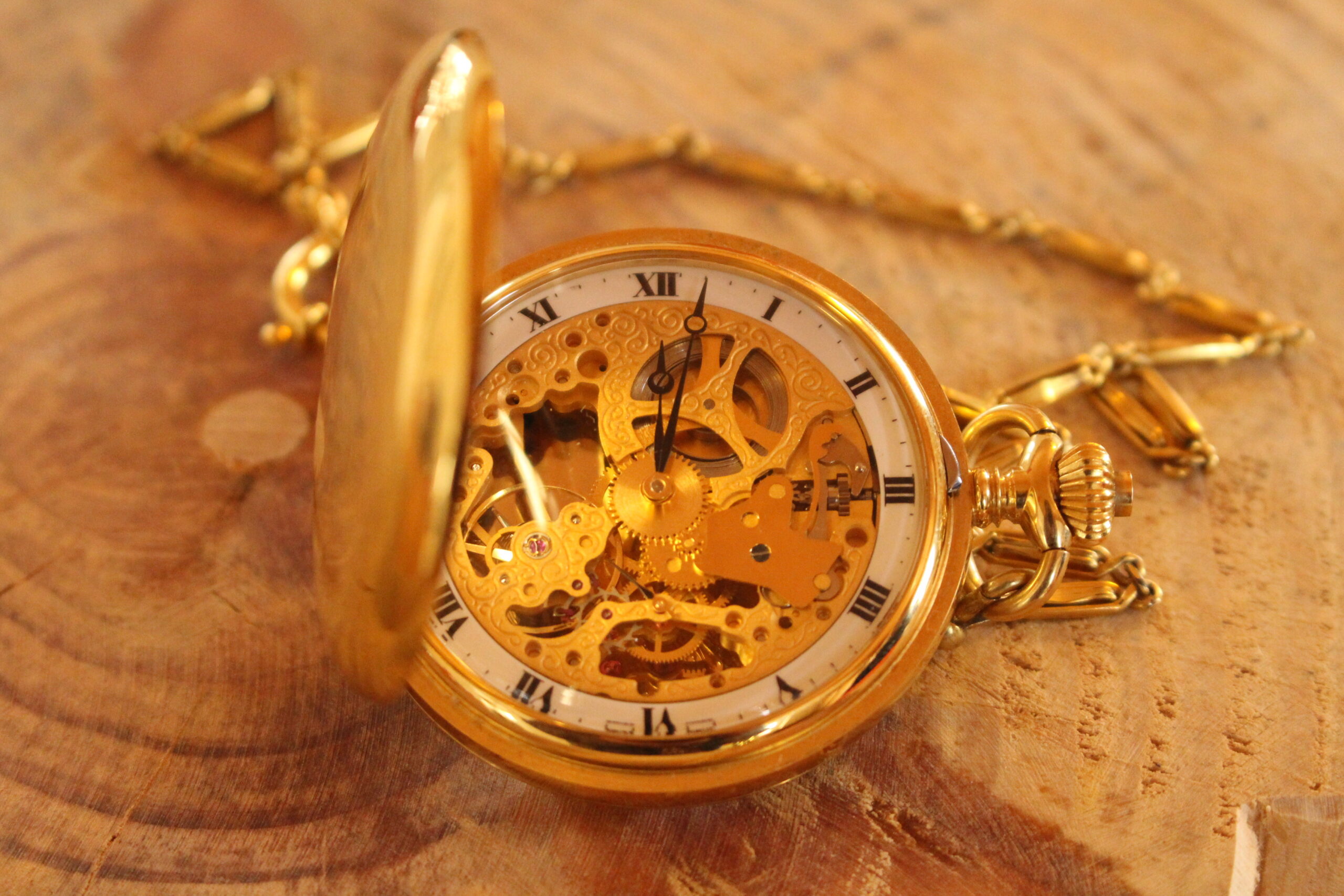 Eine goldene Taschenuhr liegt aufgeklappt auf einem Tisch und das Ziffernblatt sowie die dahinterliegende Mechanik sind zu sehen.